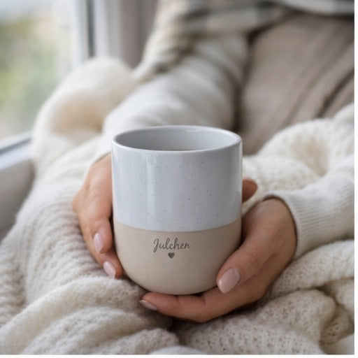 Cozy hands cradle a personalized two-tone handleless stoneware mug. Light grey and beige with "Julchen" and a heart, ideal for pregnancy reveals.